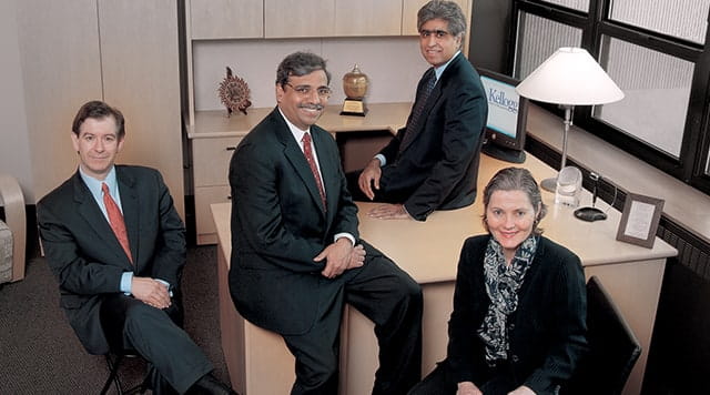 2007: 3 men, 1 woman posing together at an office desk