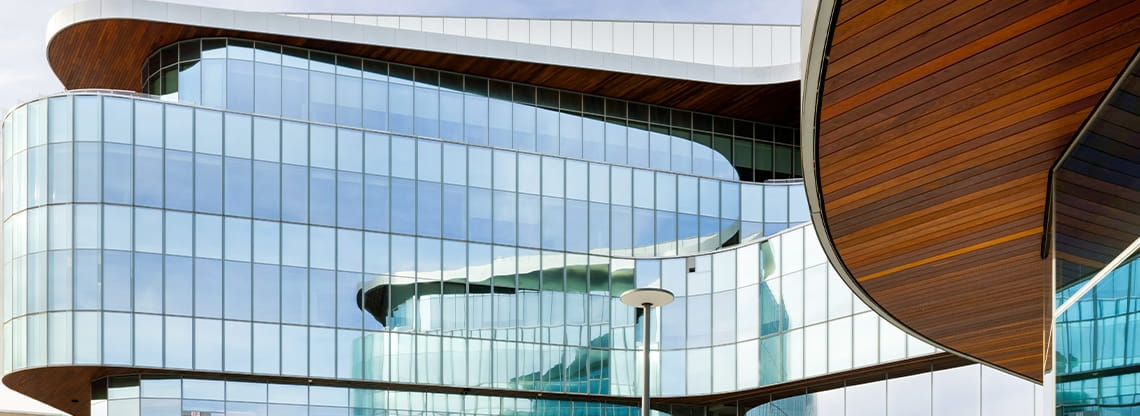 Exterior of the Kellogg Global Hub's curvilinear, blue/green glass walls with warm brown wood showing beneath the overhangs