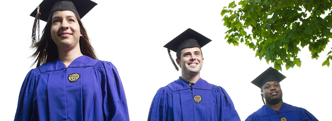 Three Kellogg graduates wearing regalia stand tall against a clear sky.