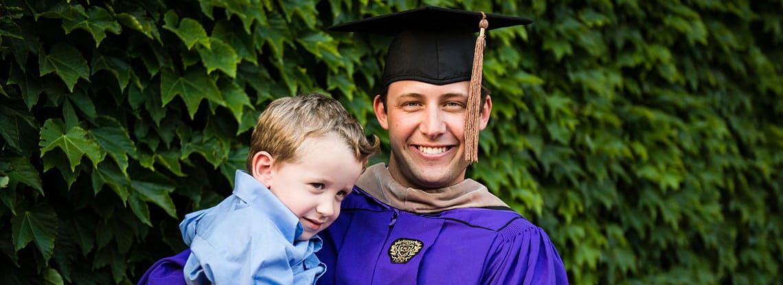 A Kellogg graduate poses with his young son against a lush background.