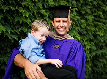 A Kellogg graduate poses with his young son against a lush background.