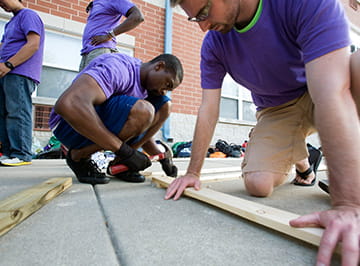 Volunteers help in construction by cutting wood.
