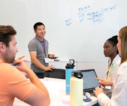 Four students working in a room while one writes on a whiteboard.