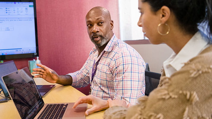 Two seated Kellogg MBA students with laptops discussing a spreadsheet