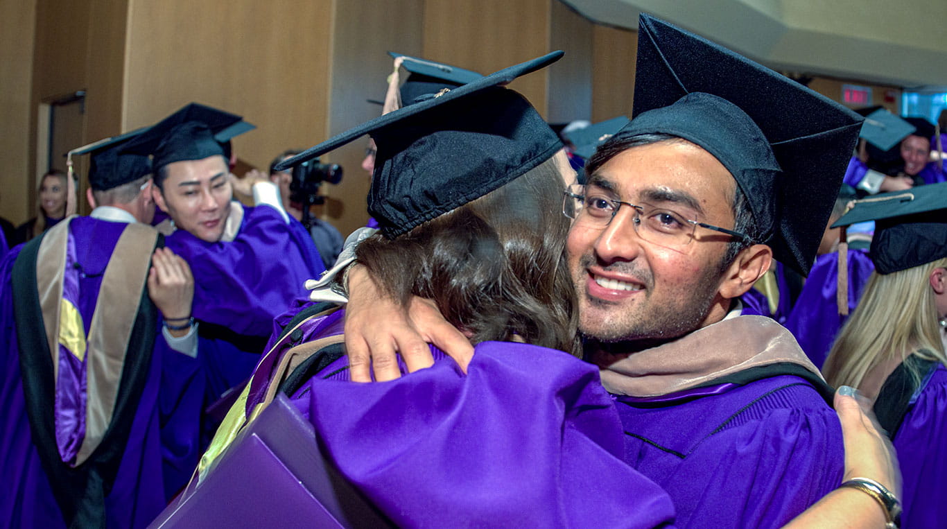 Students in purple graduation robes and hats hug and smile 