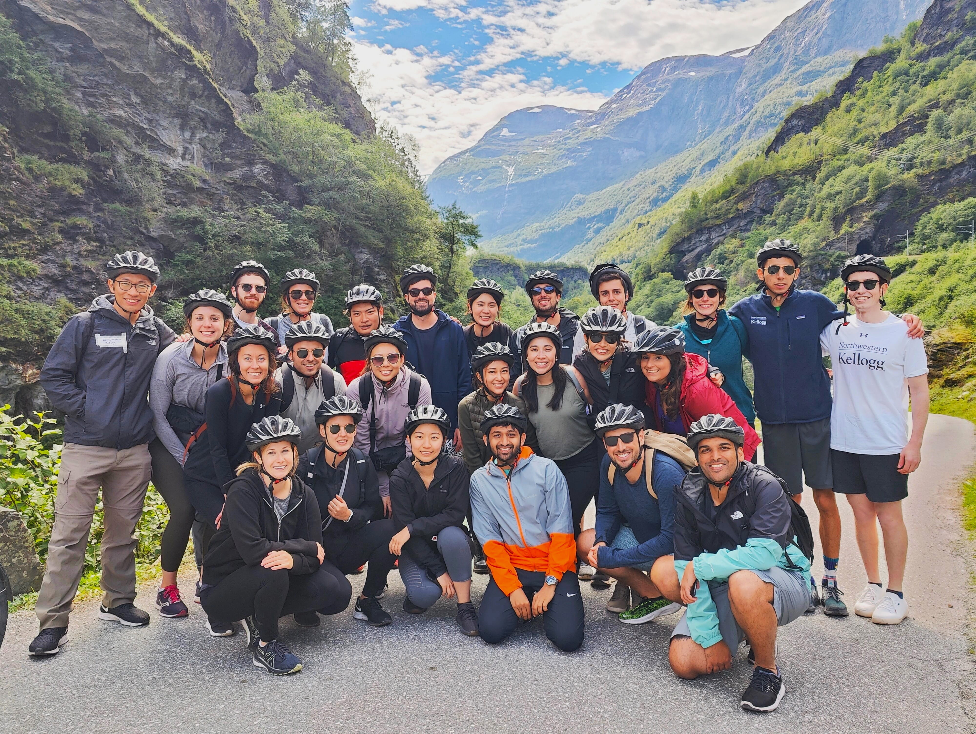 Students post for group picture in active gear and biking helmets at a mountain view point.