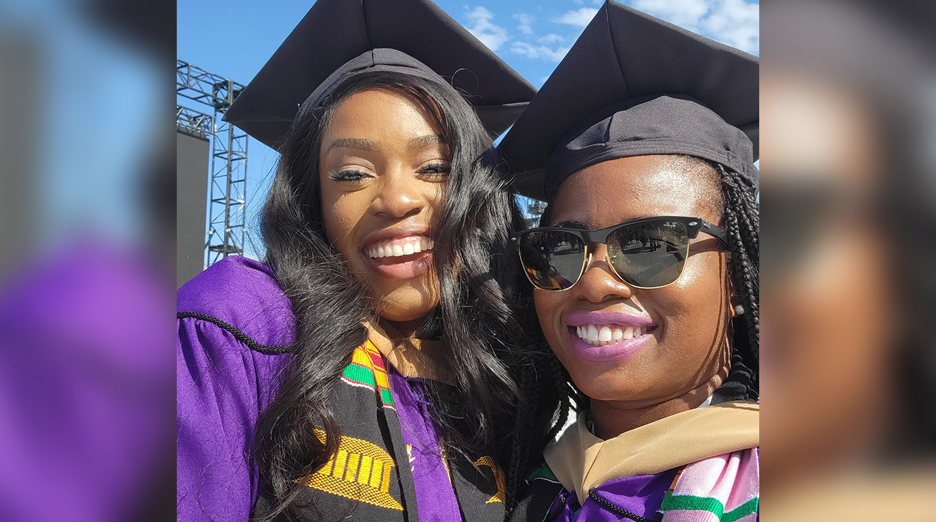 Aishley Hassell wears sunglasses and poses with a friend on graduation day, both wearing purple caps and gowns.