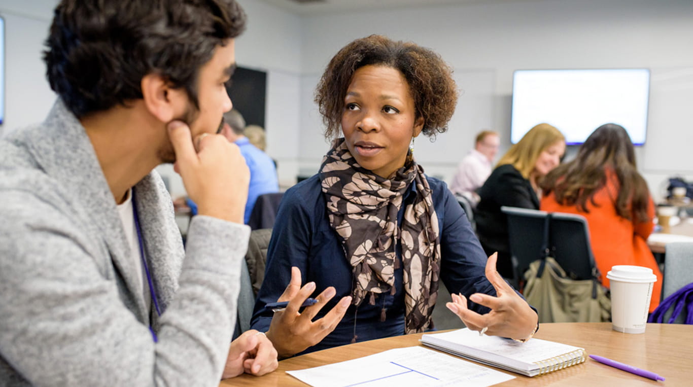 Women wearing a scarf speaks to a student who is listening intently