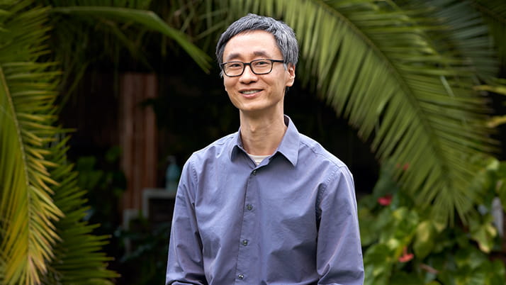 Kellogg alumnus Andrew Youn stands in front of a scenic backdrop of palm leaves and other plants