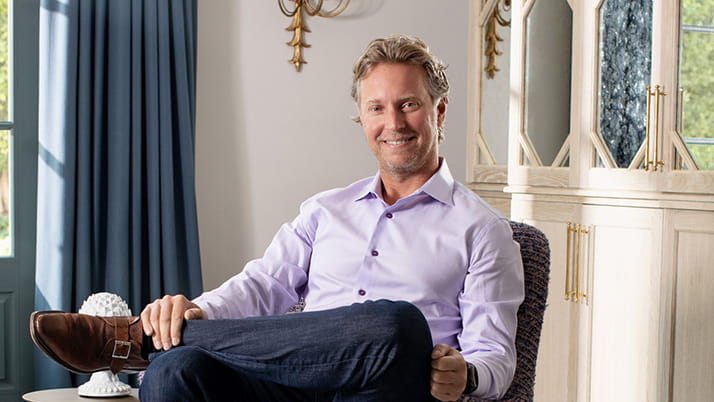 Kellogg graduate Sam Shank pictured in a room with blue curtains and a tall ivory cabinet
