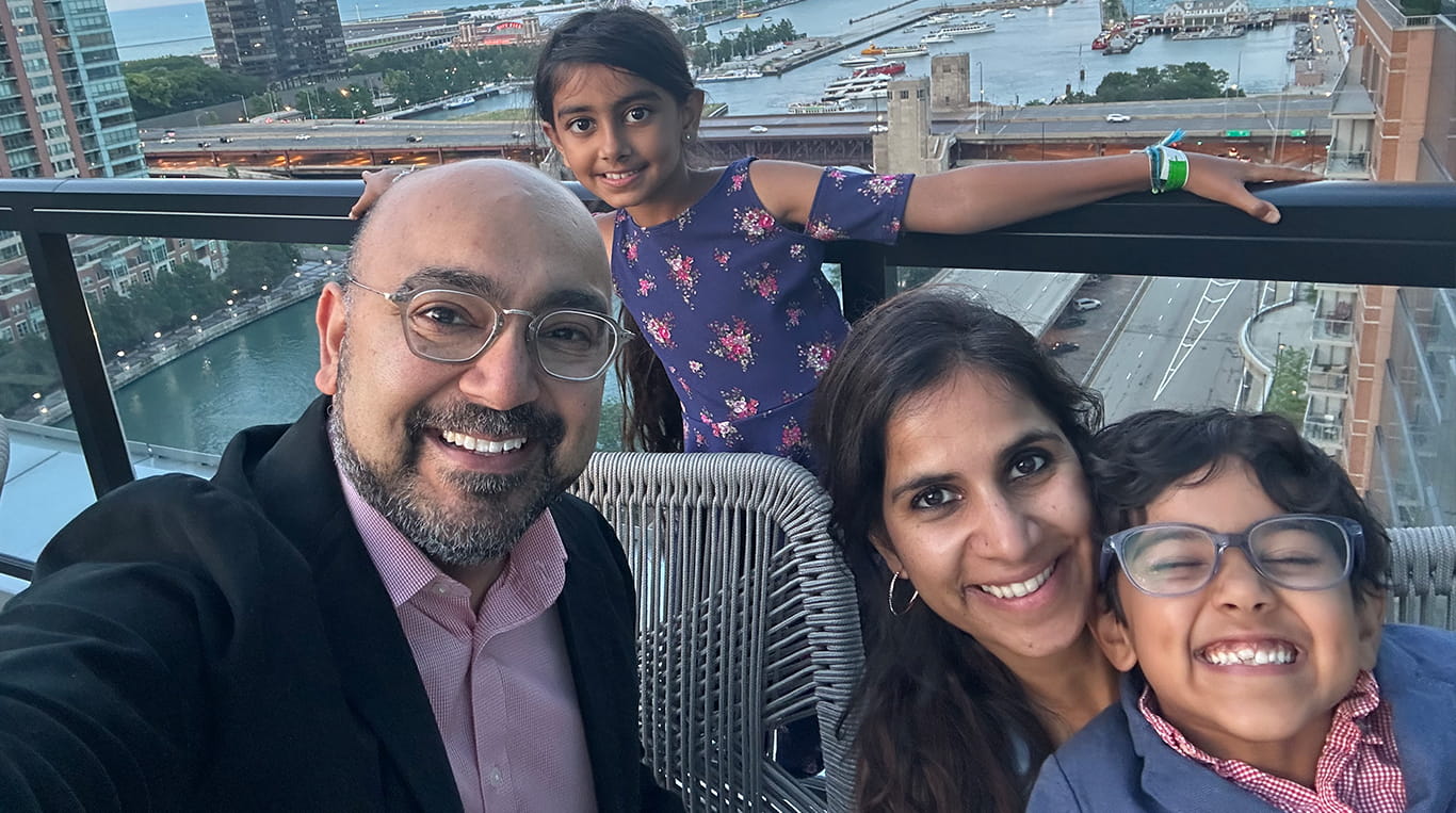 Kellogg graduate Ajit Kalra ’20 MBA and his wife Sukhu pose with their children on a balcony overlooking the downtown Chicago skyline.