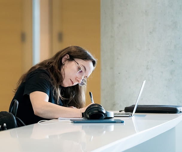 A woman sitting at a table takes notes while a laptop computer is open in front of her