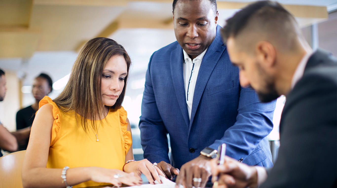 A woman and two men in business attire review a document together