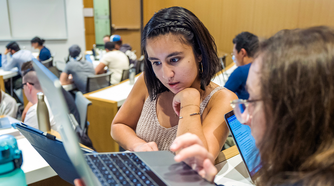 Kellogg students in a classroom collaborate on a project while looking at a laptop screen together