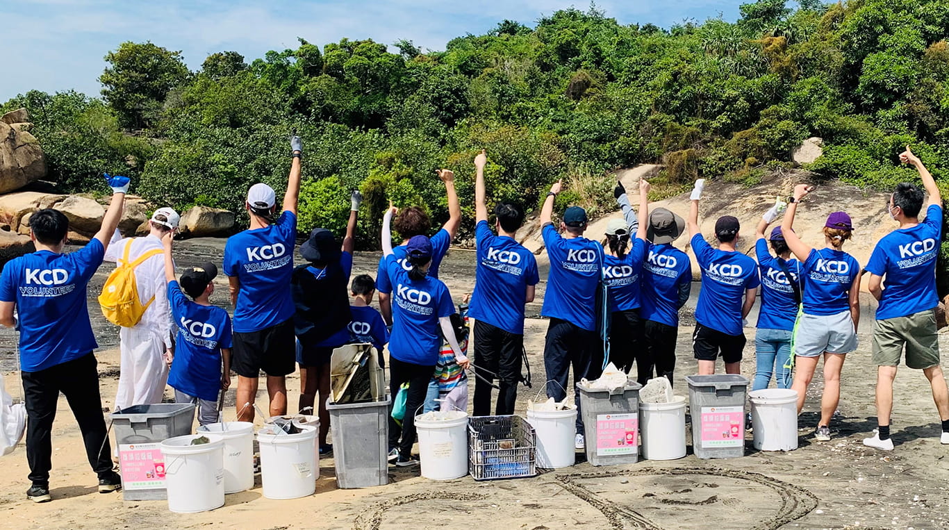 A group of alumni volunteers and their kids show off their matching t-shirts during a beach clean-up day
