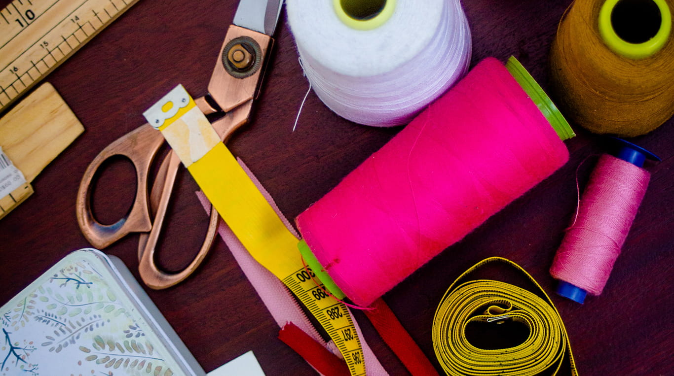 Sewing materials laid out on a table, including pink thread, a measuring tape, ruler and scissors