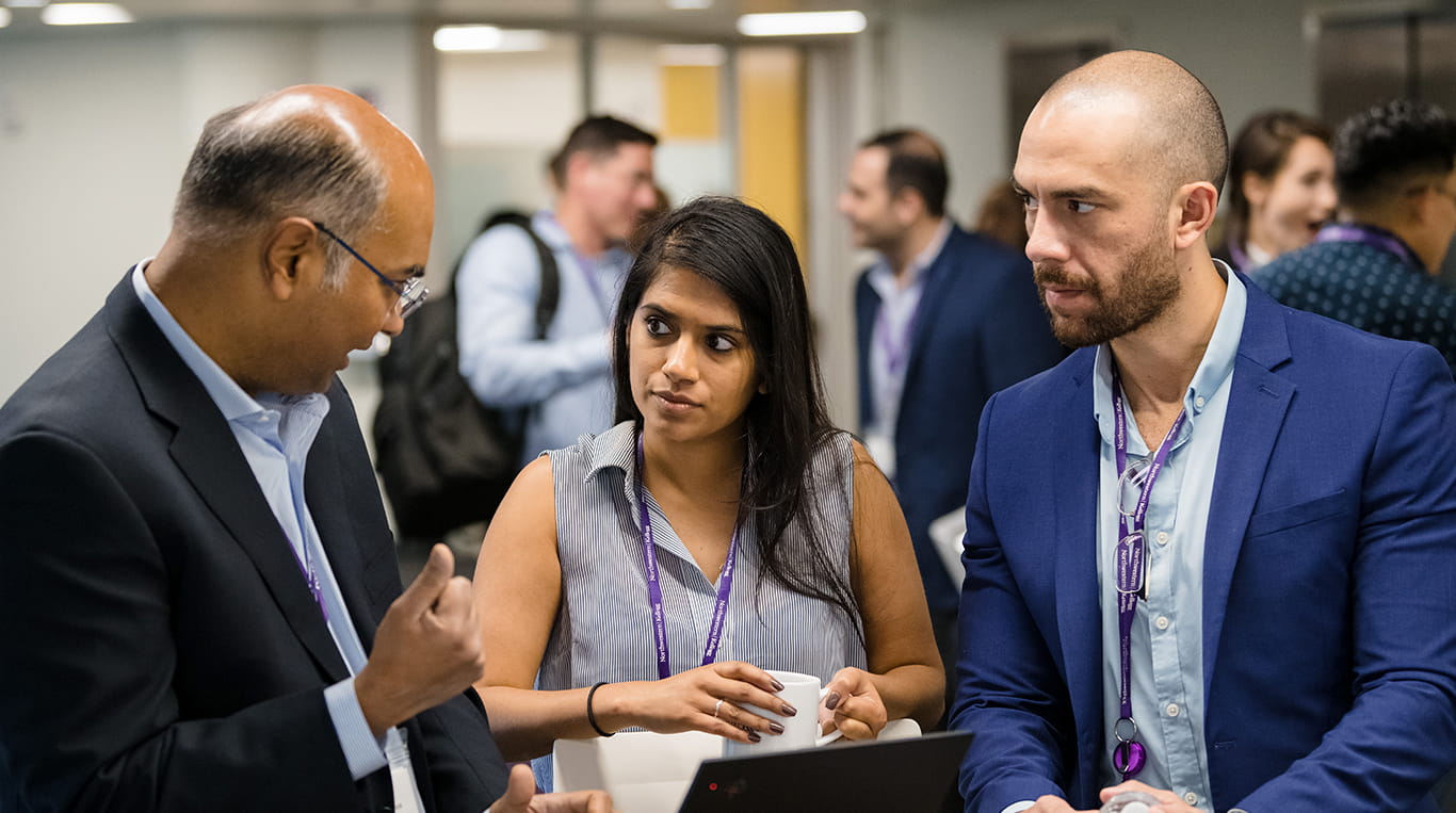 Three Executive MBA students in business attire stand together and have a conversation