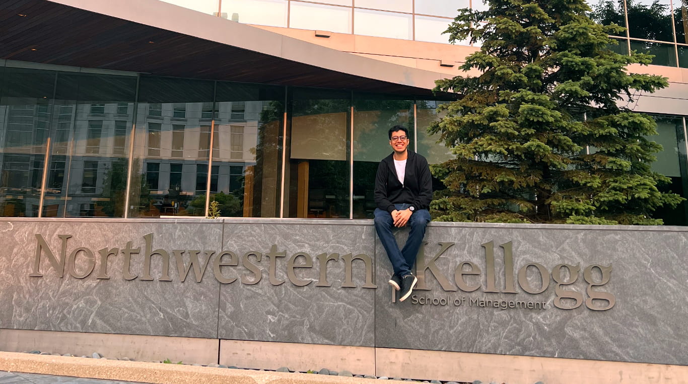 MMM student Maanil Dodani sits atop the Kellogg School of Management sign at the Global Hub.