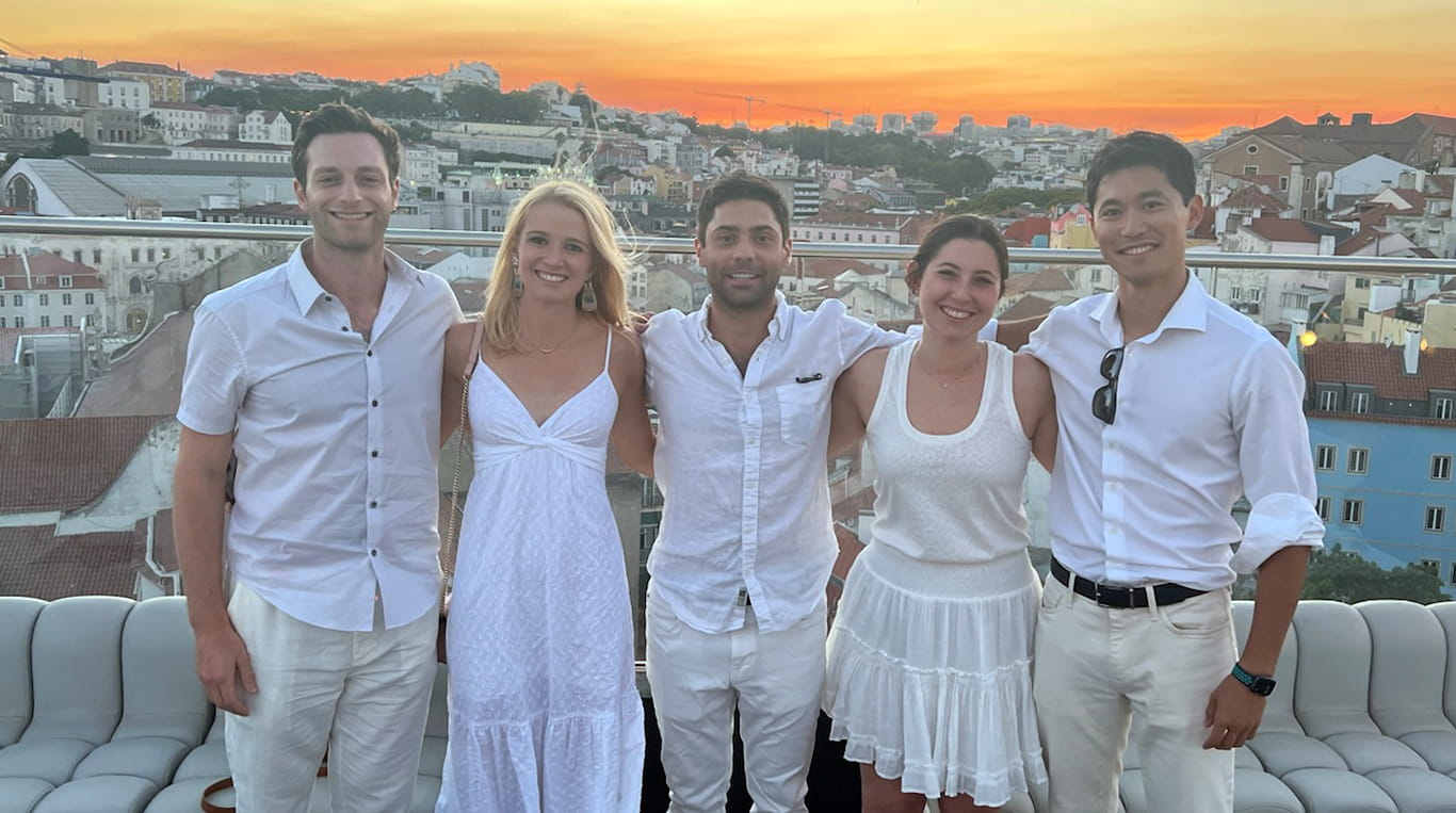 Students on a KWEST trip to Portugal wear white and stand on a balcony overlooking the town while the sun sets behind them