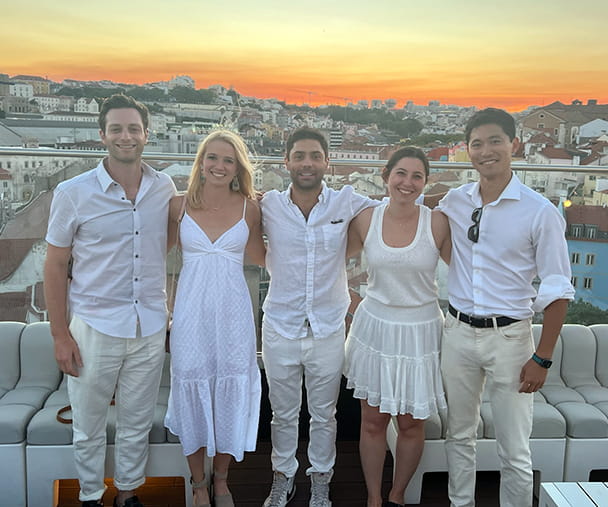 Students on a KWEST trip to Portugal wear white and stand on a balcony overlooking the town while the sun sets behind them