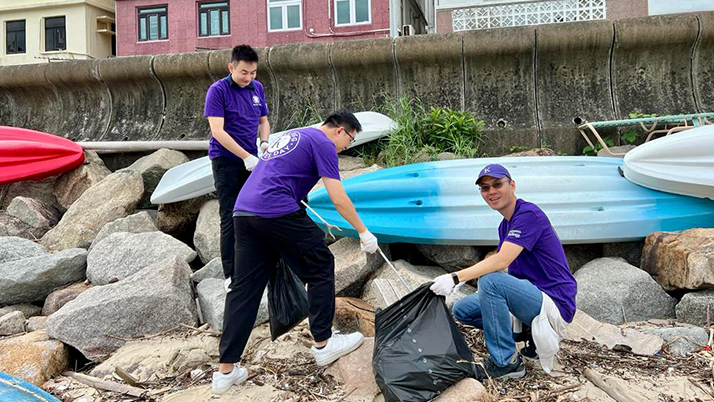 Three Kellogg alumni volunteers wearing purple shirts clean up trash from a beach