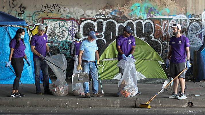 A group of Kellogg alumni clean up trash beneath a highway underpass