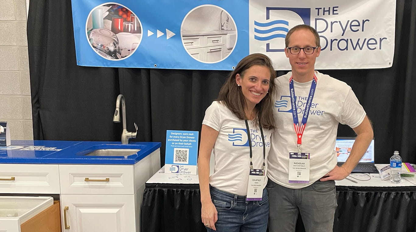 Kellogg alum Nic White-Petteruti and his wife Courtney Baron stand in front of the Dryer Drawer's booth at a trade show.