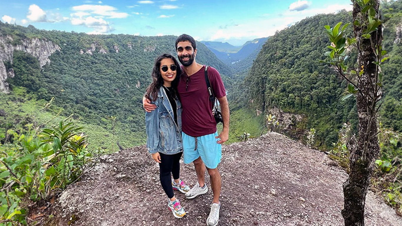 A man and a woman posing in front of a rainforest landscape