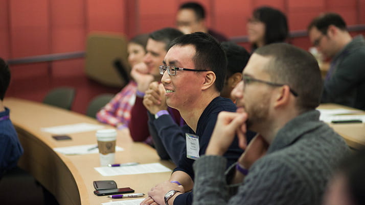 A group of Kellogg students lean forward in their chairs listening to a classroom lecture
