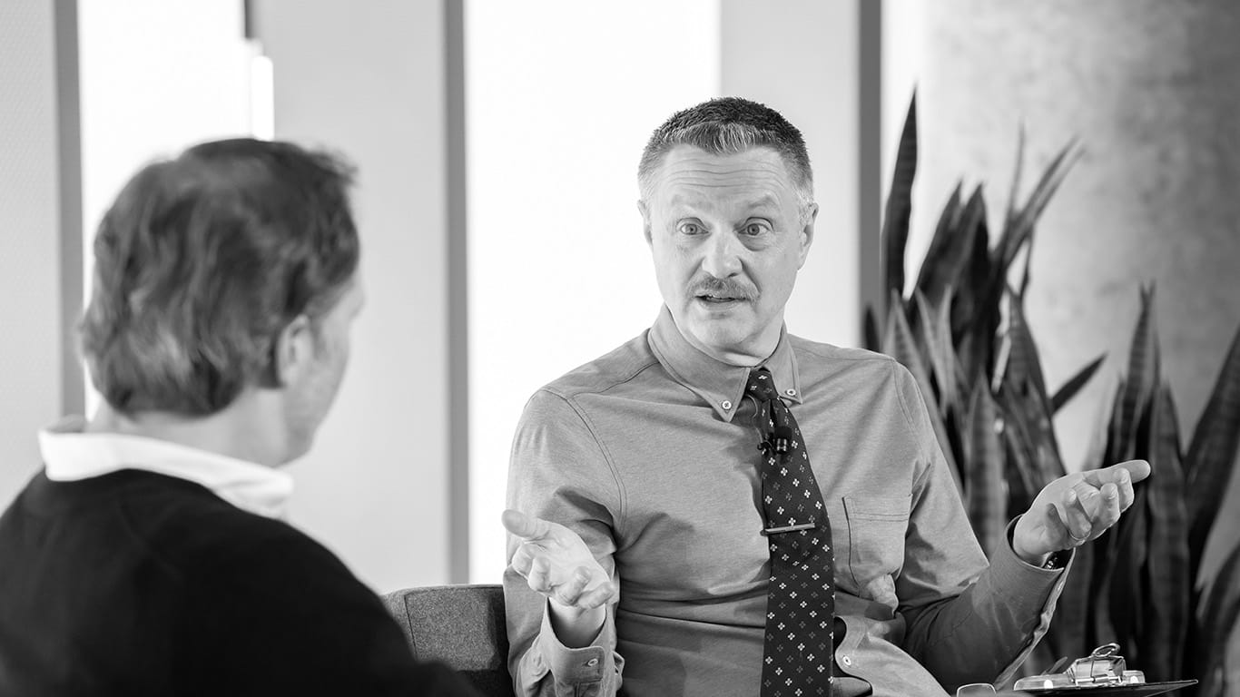 Black-and-white photograph of professor Jim Lecinski speaking to another person during a panel discussion