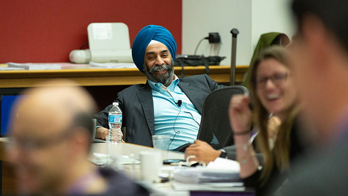 Professor Mohan Sawhney sits in a chair and leans back smiling as students around him participate in lively conversation.