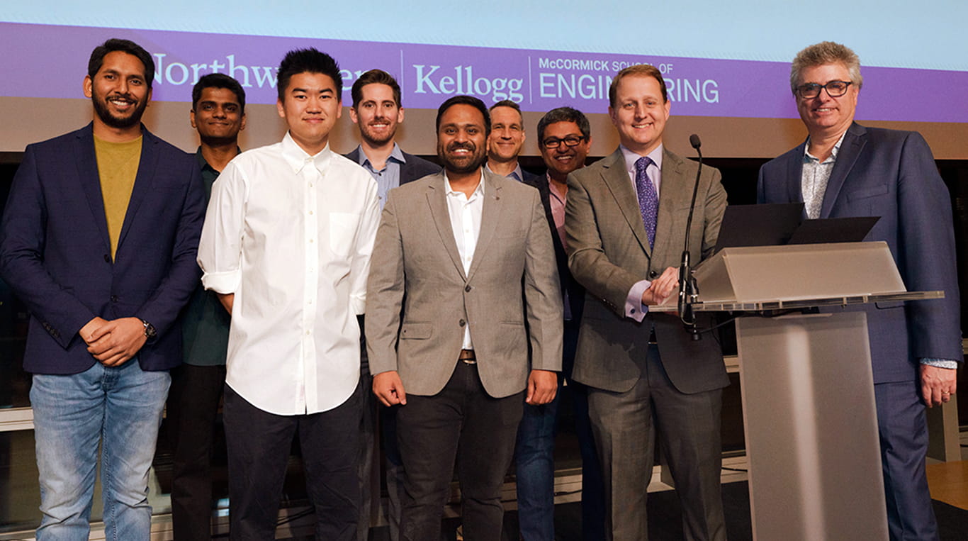 MBAi and MSAI students and faculty from Northwestern's Kellogg School of Management and McCormick School of Engineering pose together on stage after a student project showcase.
