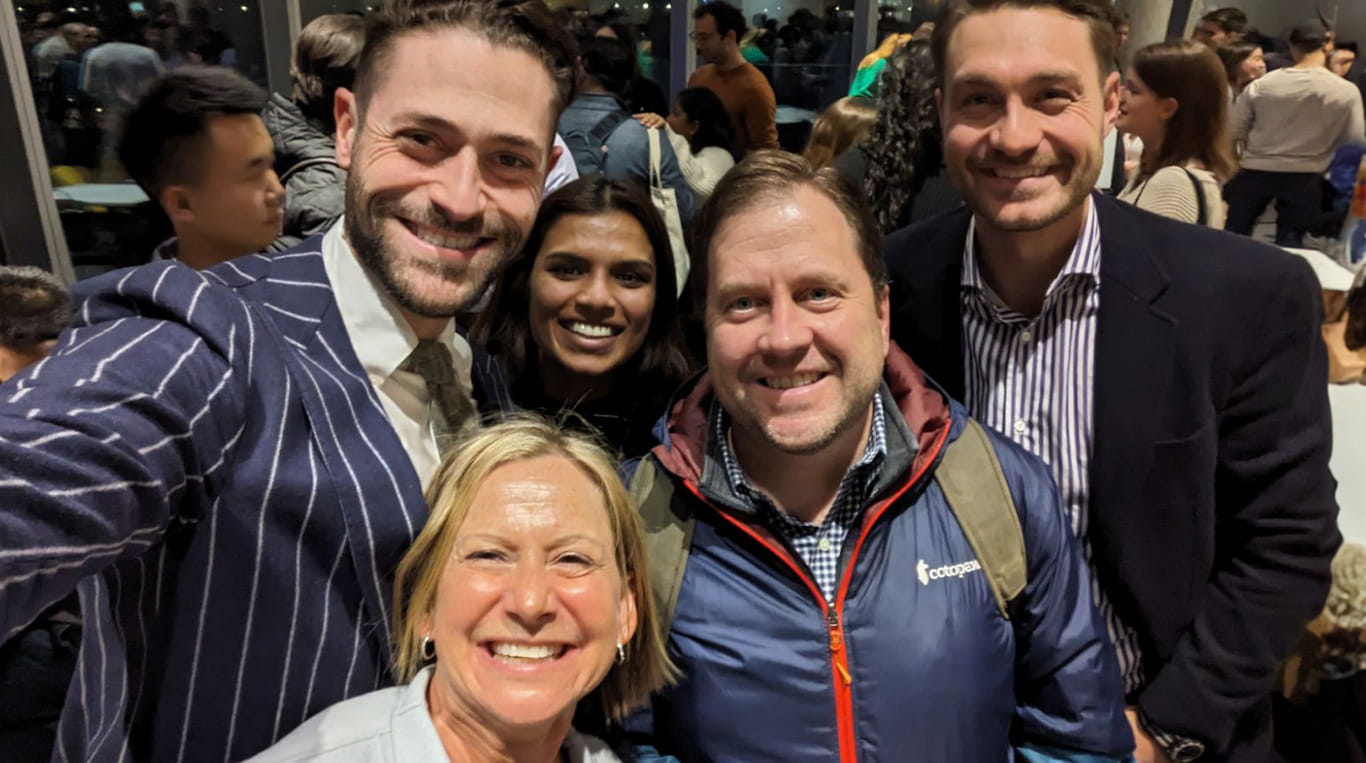 Kellogg faculty Katie Arnold and Evan Norton smile and pose for a group photo with students at a Kellogg gathering.