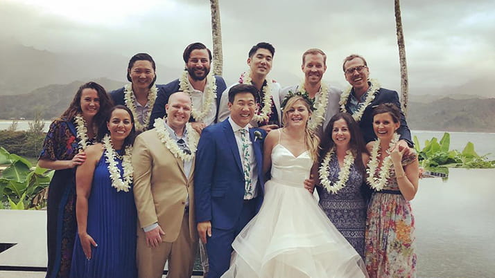 Kellogg alumna Lindsey Baker poses with other alumni at a friend's wedding. They all wear formalwear and flower leis in a tropical setting.