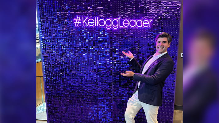 A man posing in front of a purple neon sign that says #KelloggLeader.