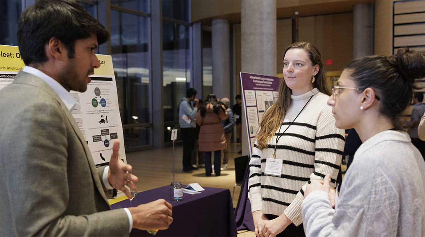 Two students stand and explain their class presentation during the MBAi Capstone showcase.