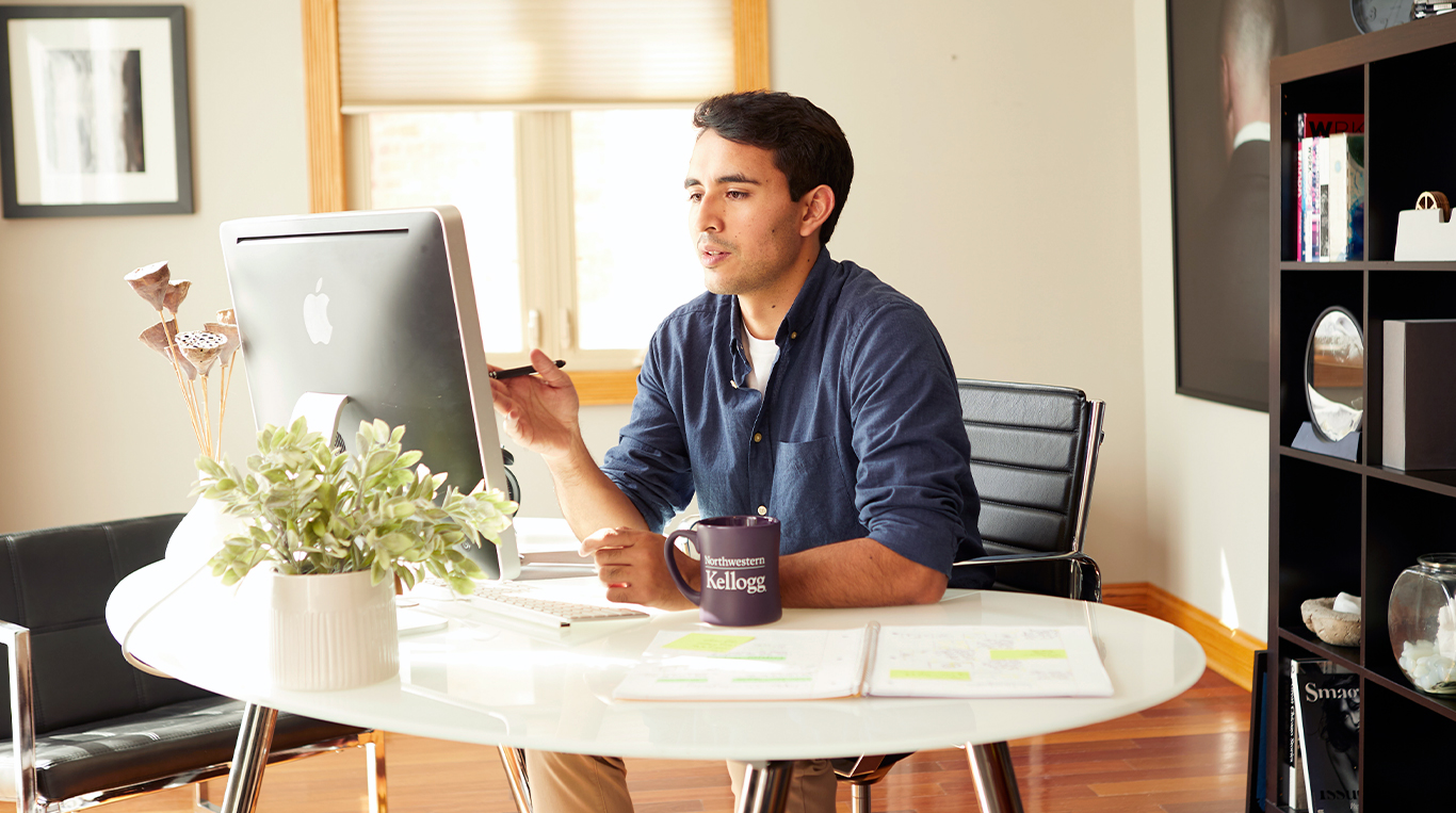 A professional participates in a virtual meeting or class, fully engaged from a modern, well-lit home office. With a Northwestern Kellogg mug by his side, notes on the table, and a stylus in hand, he exemplifies focused learning and remote productivity—hallmarks of today’s flexible business education.
