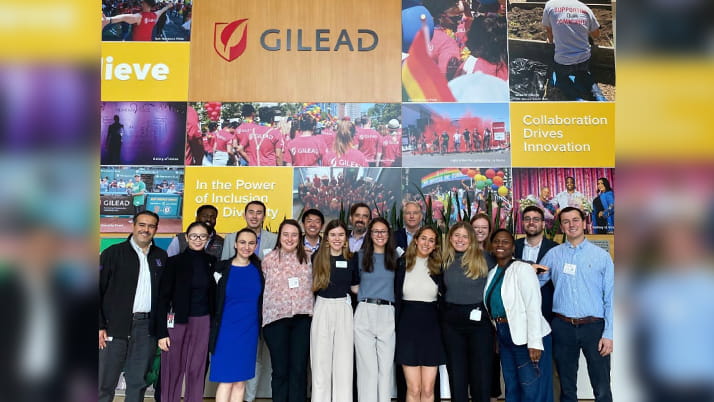 A group of Kellogg students pose in front of a colorful lobby display at a Gilead Sciences building, while on a visit to the biopharma company.