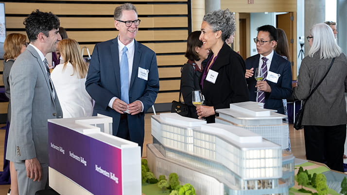 Attendees at the groundbreaking ceremony stand and chat near a small scale model of the new building.