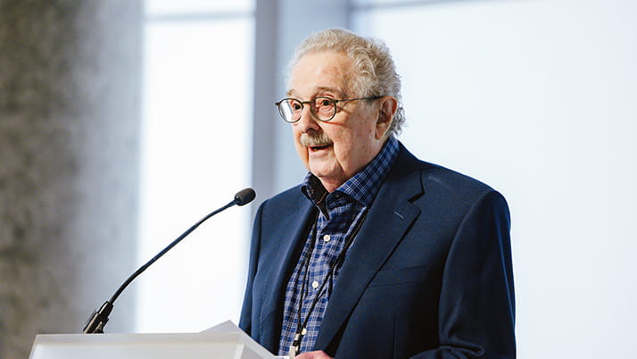 Ward Center founder Lloyd Shefsky speaks at its re:connect conference, wearing a navy blazer and blue checkered shirt, standing behind a podium.