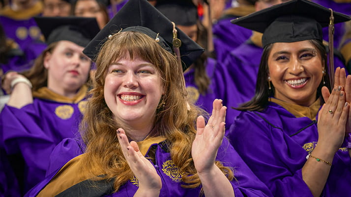 Graduating Kellogg students wear purple gowns and black caps, and applaud from the crowd during convocation ceremonies.