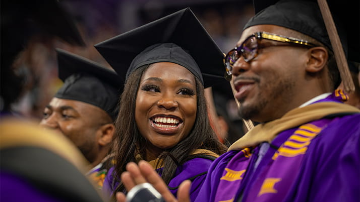 Kellogg graduates wearing purple gowns and black caps smile and applaud during the convocation ceremony.