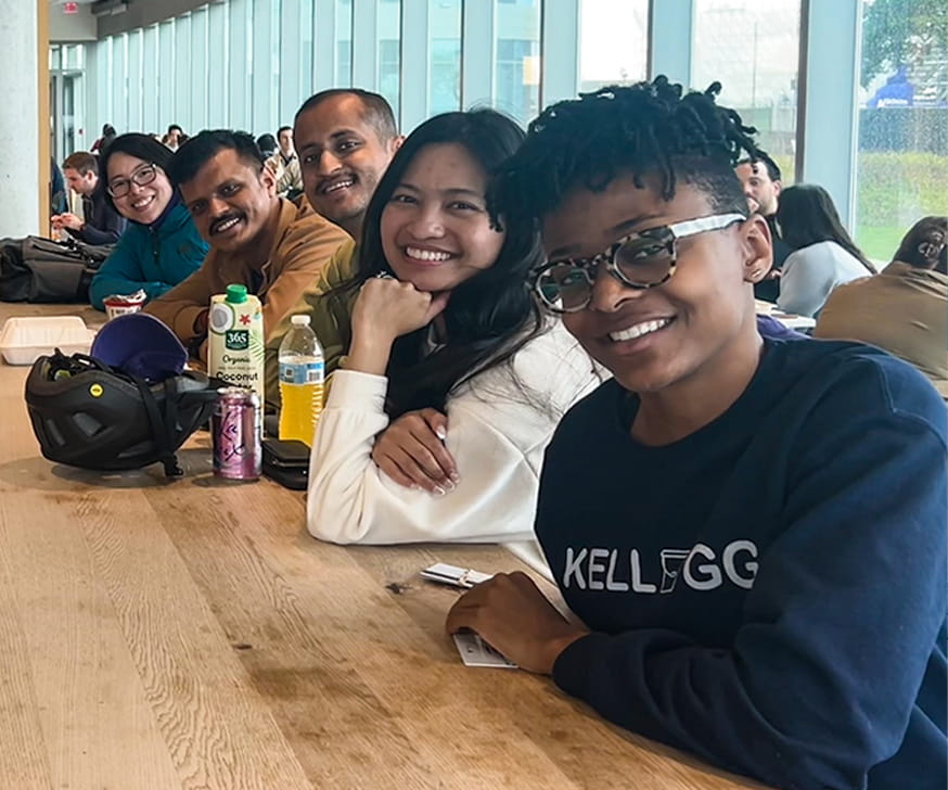 An African American female MBA student sitting with her peers at a table at the Global Hub's cafeteria.