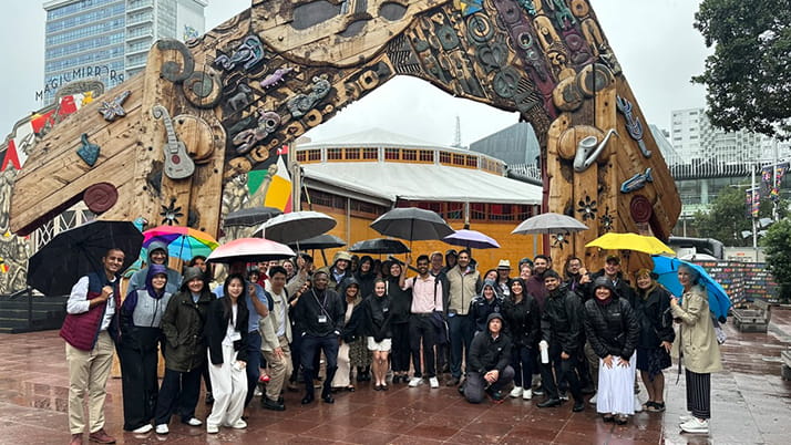 A group of MBA students standing in the rain with umbrellas at a plaza in New Zealand.
