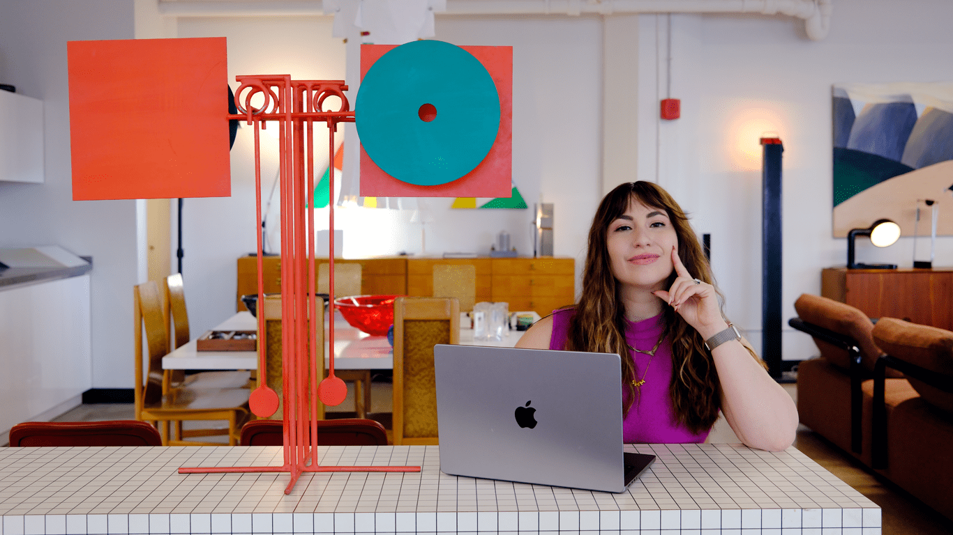 A woman sitting in next to an orange table top frame with an open laptop in front of her.