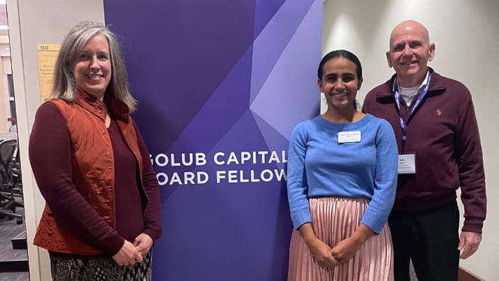 Three people stand in front of a purple banner that reads “Golub Capital Board Fellows.” They are smiling at the camera inside a professional setting.