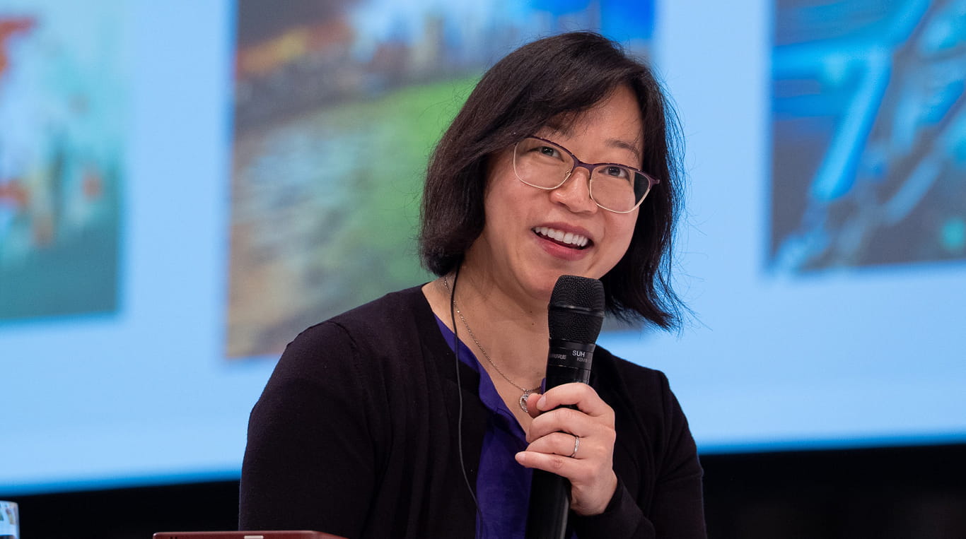An Asian woman wearing glasses holding a mic