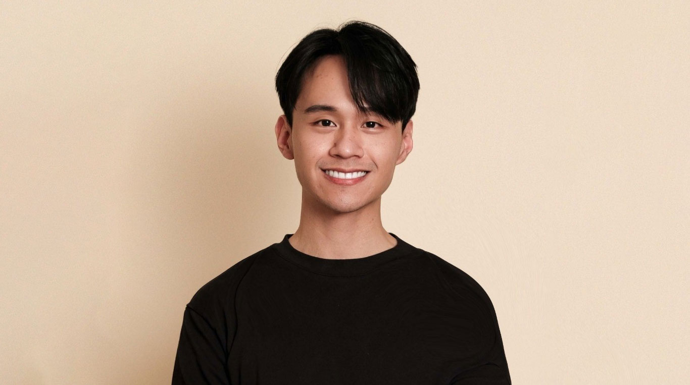 Kellogg MBAi student Will Tan smiles, wearing a black shirt and standing against a tan background