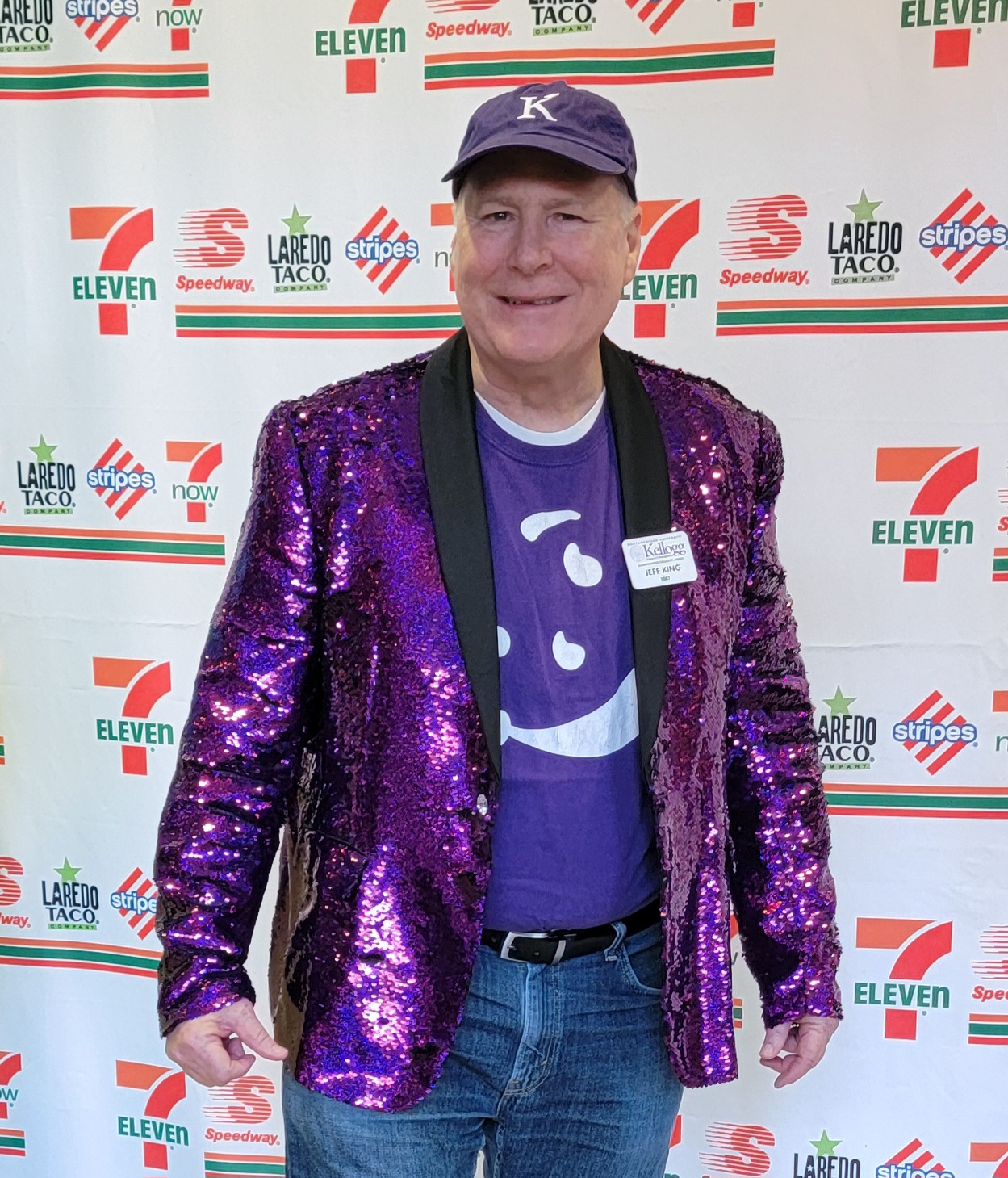 A white man wearing a sparkly purple blazer and a hat.