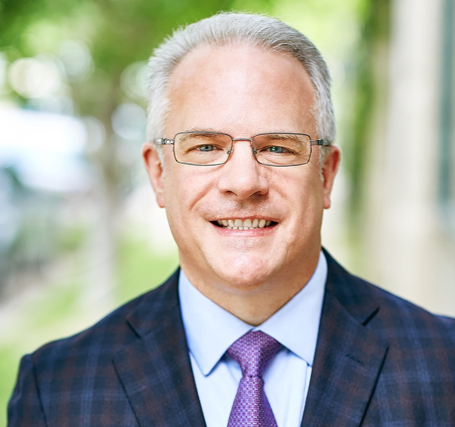 A white-haired white man wearing glasses and a navy houndstooth sport jacket.